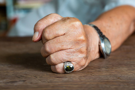 老人左手握拳在木桌背景上,痣和瑕疵,特写和宏拍,选择性聚焦,亚洲身体