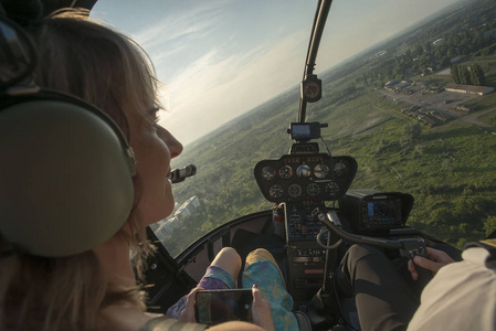 美丽的金发女子在直升机上用智能手机拍摄城市景观.