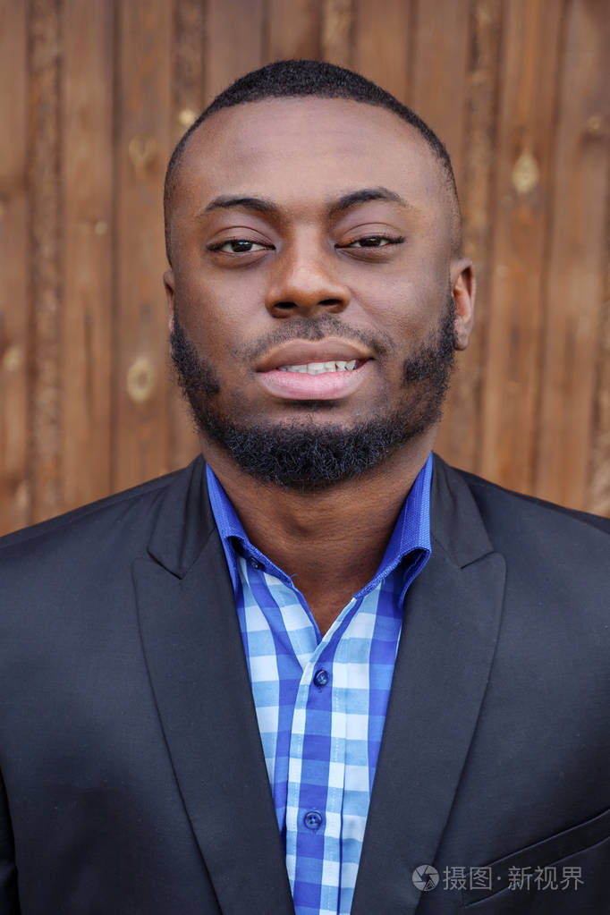 身着西装的美国黑人男子微笑着看着深色木头背景上的相机