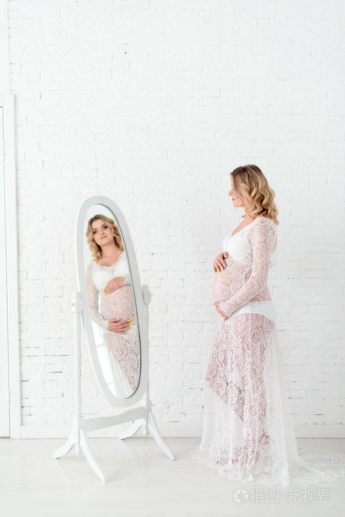 美丽的怀孕的金发女人抱着他的肚子在光书房照片-正版商用图片2m9izr