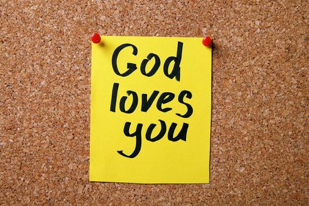 一张写着上帝爱你的纸挂在软木板上照片