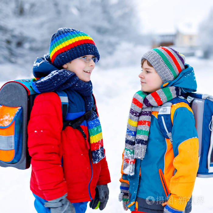 两个小学的小男孩在下雪时步行去上学.快乐的孩子们在玩第一场雪.
