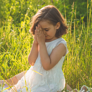 美丽的夕阳下,小女孩闭上眼睛,在田野里祈祷双手合十祈祷信仰照片