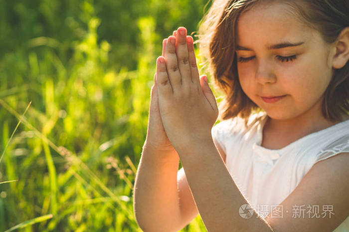 美丽的夕阳下小女孩闭上眼睛在田野里祈祷双手合十祈祷信仰