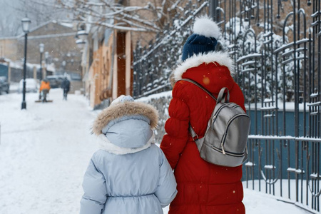 两个女孩走在城市里冬天的雪地街道上,孩子们正牵着手,背影远眺照片