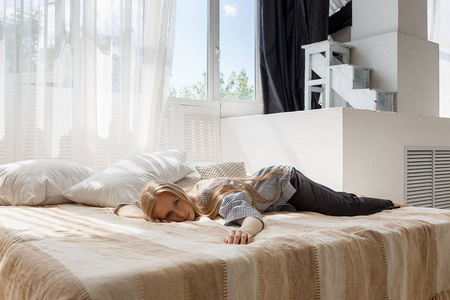 一头长发,穿着条纹衬衫和黑色裤子,脸朝下躺在摄影棚的床上,看着镜头