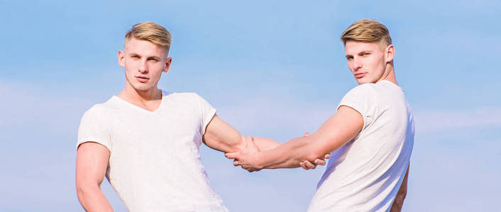 友谊和支持.男人肌肉发达的双胞胎兄弟穿着白衬衫天空背景.