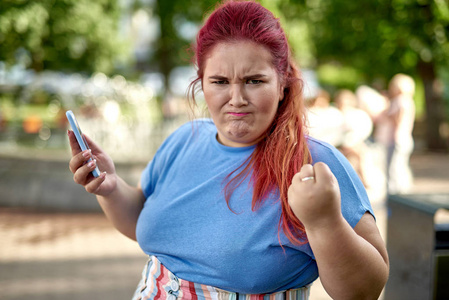 年轻胖女人做鬼脸,拿着智能手机照片