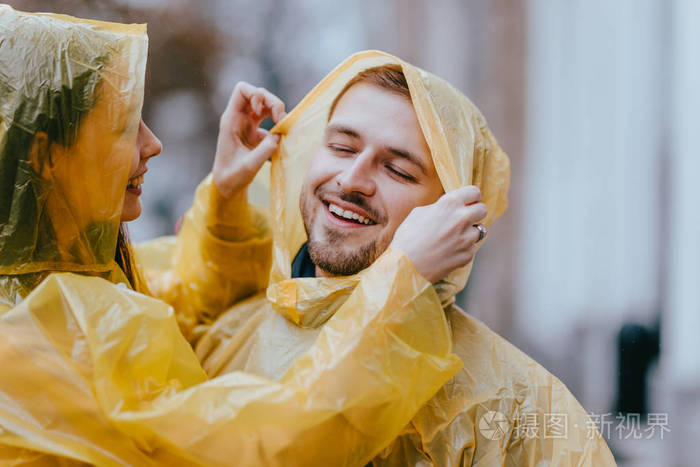 一对幸福的情侣盖伊和穿着黄色雨衣的女友在雨中拥抱在街上