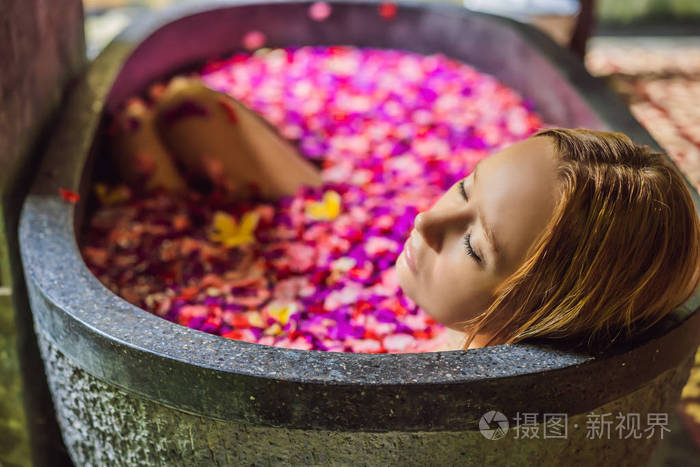 迷人的年轻女子沐浴着热带花朵的花瓣和芳香油.水疗治疗皮肤恢复活力.