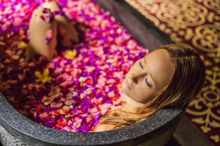 迷人的年轻女子沐浴着热带花朵的花瓣和芳香油.水疗治疗皮肤恢复活力.