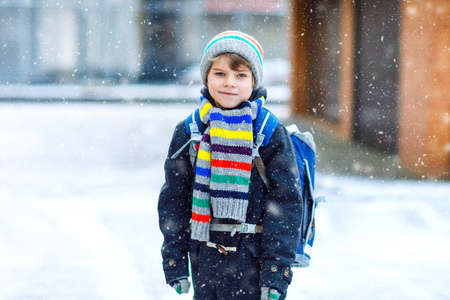 带背包或书包的学生在五颜六色的冬天衣裳小学生在下雪的时候步行上学