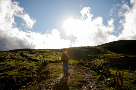 背着远足背包和拐杖在山路上行走的后视男子照片