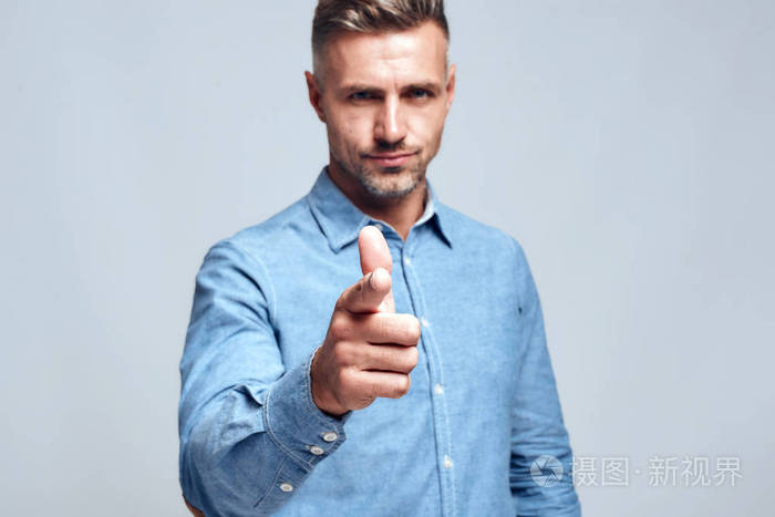 你是谁穿着蓝色衬衫的严肃帅哥站在灰色背景下用手指指着你看着摄像机