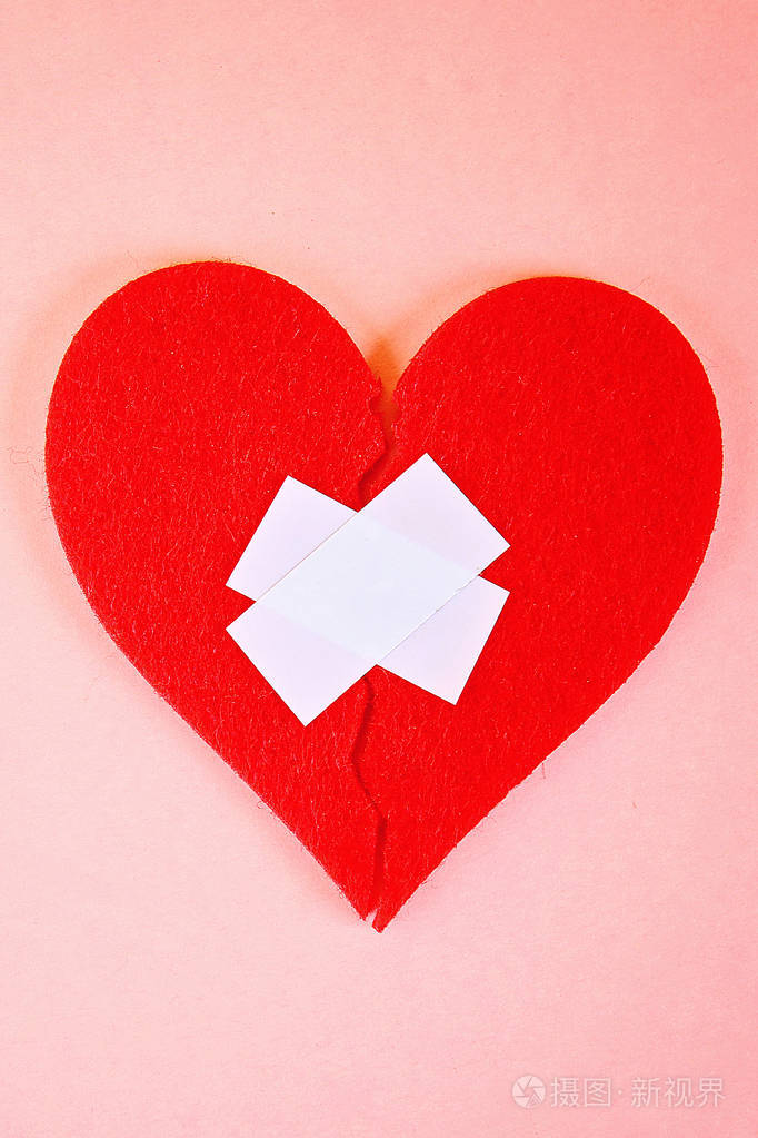 一颗红色的心碎成两半用石膏粘在粉红色的背景上
