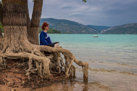 坐在湖边一棵树上沉思的女人照片