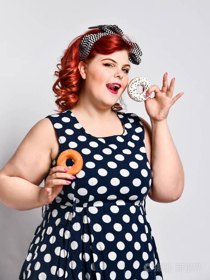 一幅美丽欢快的胖胖大号女人的画像穿着一件圆点连衣裙隔着浅色背景吃