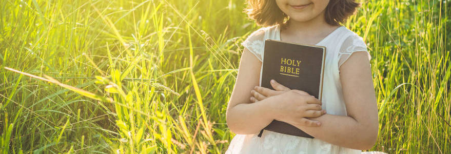 基督教女孩手里拿着圣经.在美丽的夕阳下,在田野里读圣经.