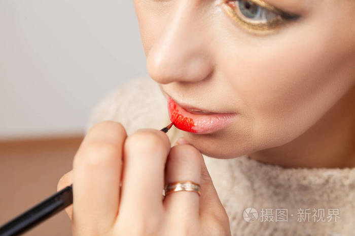 Closeup applying on the lips, the makeup artist holds a brush 
