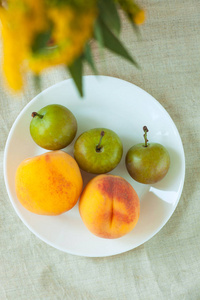 木桌上亚麻布背景的静物与新鲜桃子和李子.鲜亮多汁的夏季水果,扁桃.