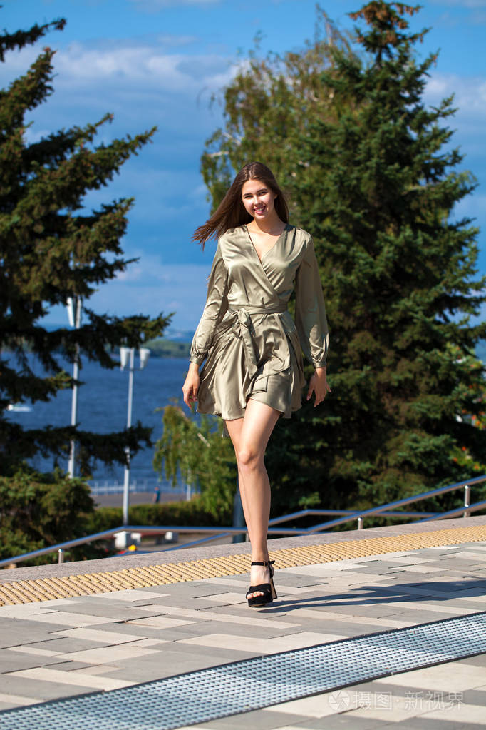 穿着绿裙子的年轻漂亮女人走在夏日的街道上