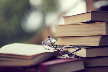 桌上放着一摞古书,玻璃杯和一本打开的书.