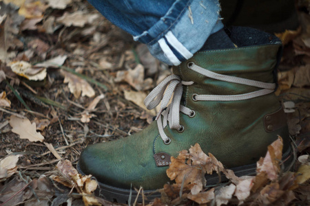 森林系在秋天的森林里,一只脚穿着绿色登山靴,脚上系着鞋带,背景是