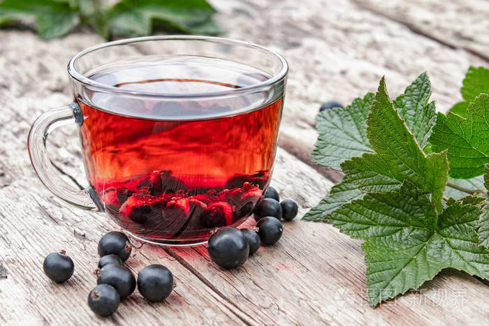 一杯红茶放在一张木桌上旁边是绿叶和醋栗浆果