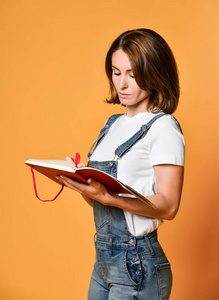 年轻漂亮的美女站着,写字,做笔记,手里拿着课本笔记本和笔照片