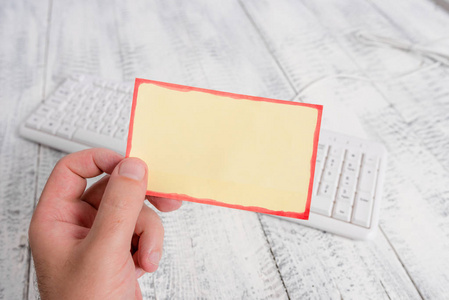 浅色木地板男人手里拿着一张空的长方形纸条,背景是白色的键盘和一块