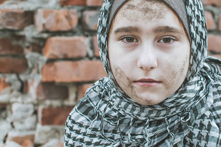 一个在战争中的难民儿童,一个满脸脏兮兮的穆斯林女孩站在废墟上,抱着