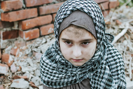 一个在战争中的难民儿童,一个满脸脏兮兮的穆斯林女孩站在废墟上,抱着