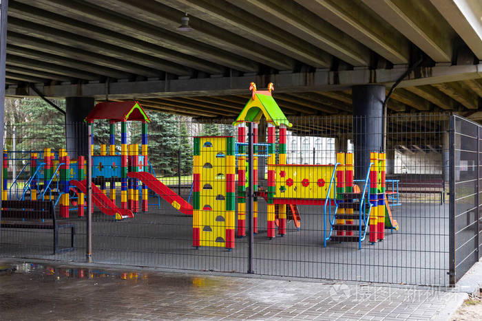 Empty kids playground under the road bridge with metal fence