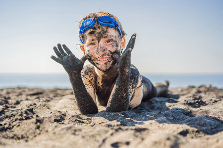 一个满脸脏兮兮的笑脸男孩在海里游泳前,坐在黑沙滩上玩耍.