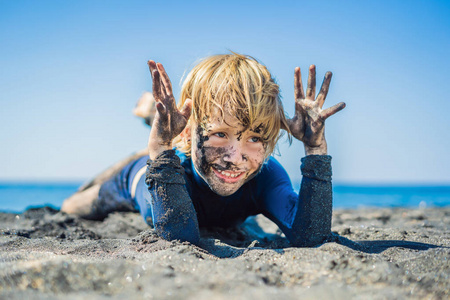 一个满脸脏兮兮的笑脸男孩在海里游泳前,坐在黑沙滩上玩耍.