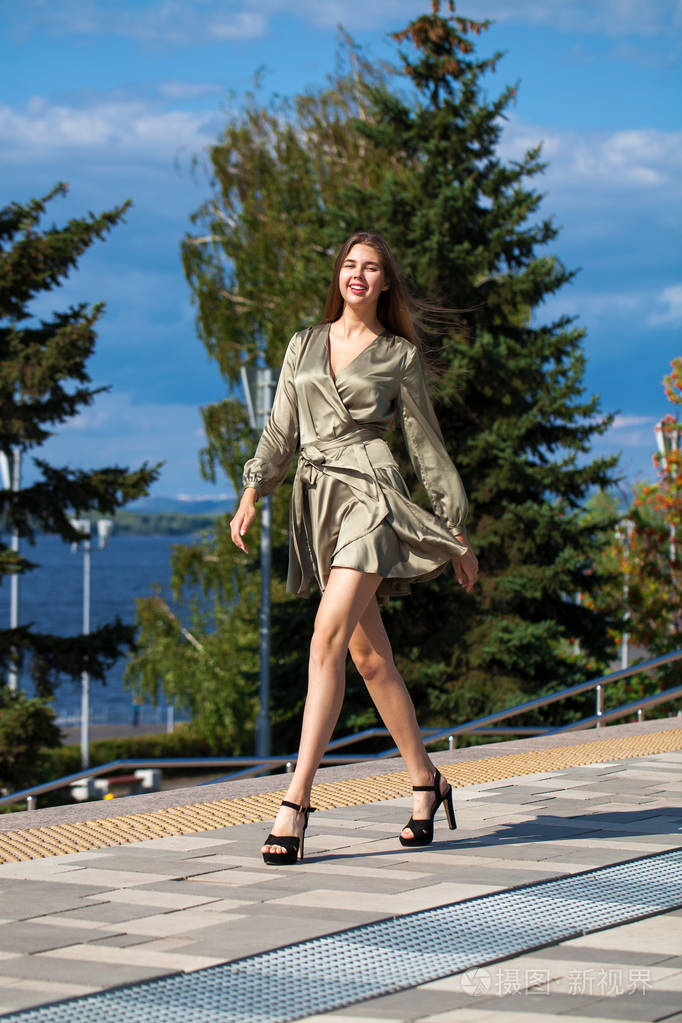 穿着绿裙子的年轻漂亮女人走在夏日的街道上