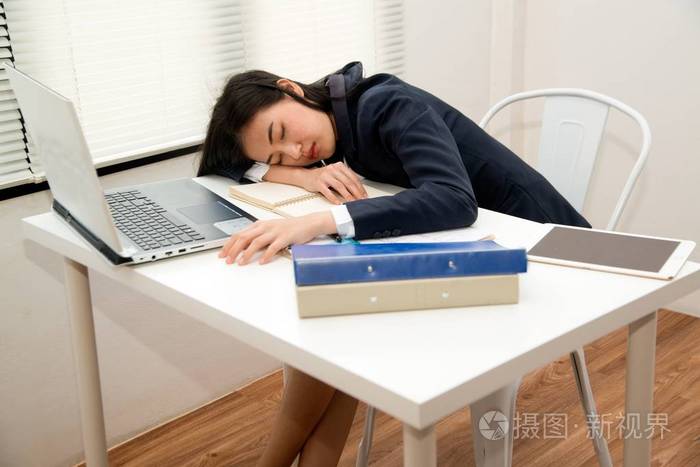 年轻的亚洲女商人因为劳累过度而躺在办公室的办公桌上