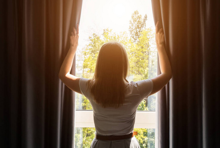 阳光明媚的早晨,女人在酒店房间里拉开窗帘.照片