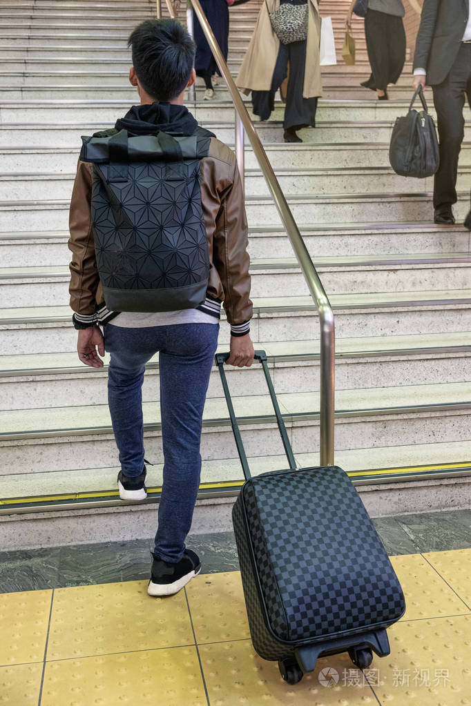 在地铁楼梯上拖着棋盘式行李的男旅客