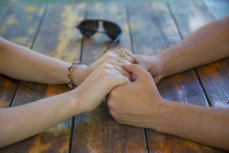 特写两个年轻的情侣手牵手在一张桌子上.手牵着手,在木桌上一起祈祷.