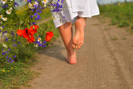 可爱的小女孩带着花环在草地上农场.她光着脚,手里拿着一束野花照片
