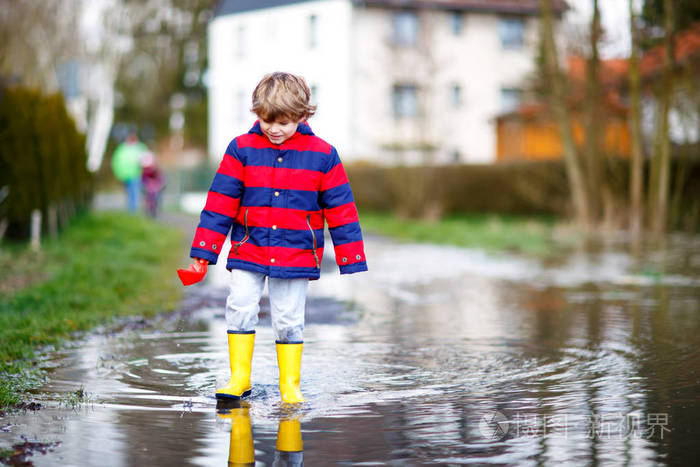 春天或秋天快乐的小男孩穿着黄色的雨靴在大水坑边玩纸船儿童活动休闲