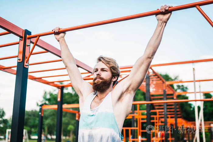 在单杠上做引体向上的强壮运动员在公园的单杠上做引体向上的肌肉男