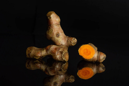 在黑色玻璃上分离的明亮的姜黄根状茎照片
