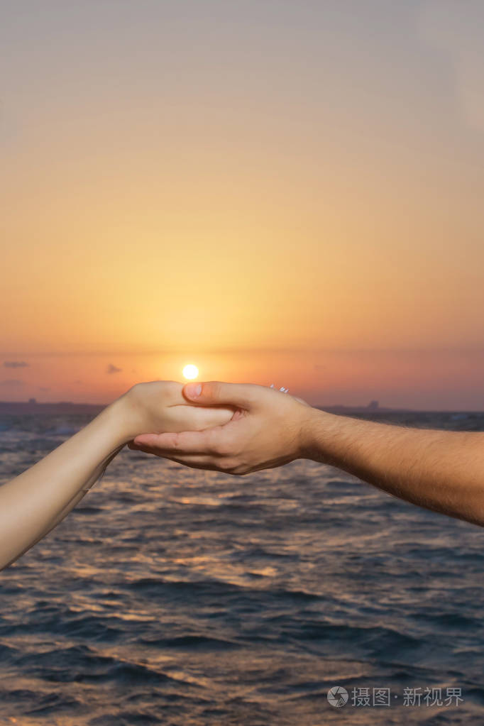 在太阳和天空的背景下牵手湖面上的手和太阳的手日落