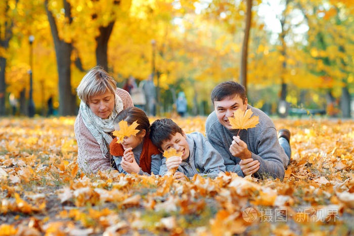 幸福的一家人躺在落叶上,在秋天的城市公园里玩耍和玩耍.
