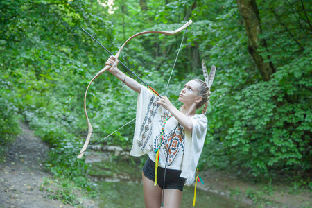 长着美洲印第安人羽毛的漂亮女孩手持弓箭照片