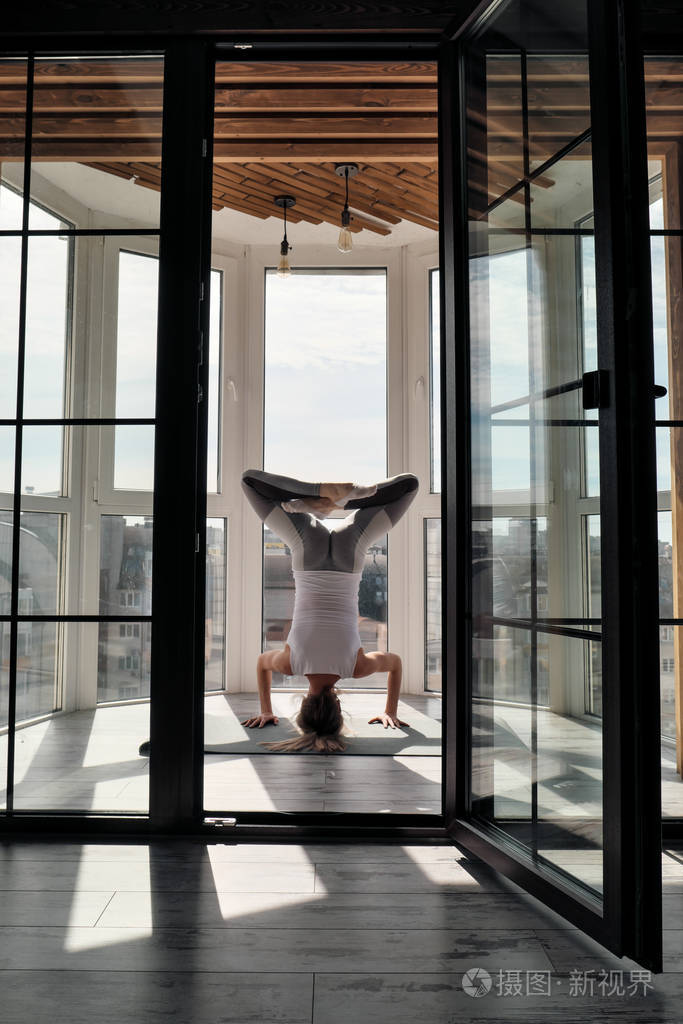 年轻漂亮的运动女性金发碧眼穿着白色运动服在家里的阳台上做瑜伽和