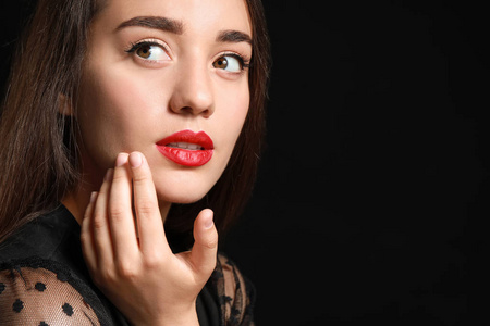 美丽的年轻女人在黑暗的背景下涂上明亮的口红照片