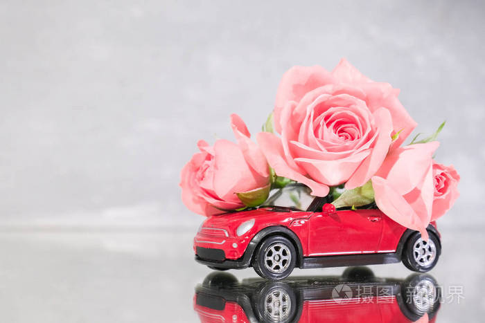 红色玩具车在灰色背景上送上一束粉红色的玫瑰花镜面反射文本的位置2